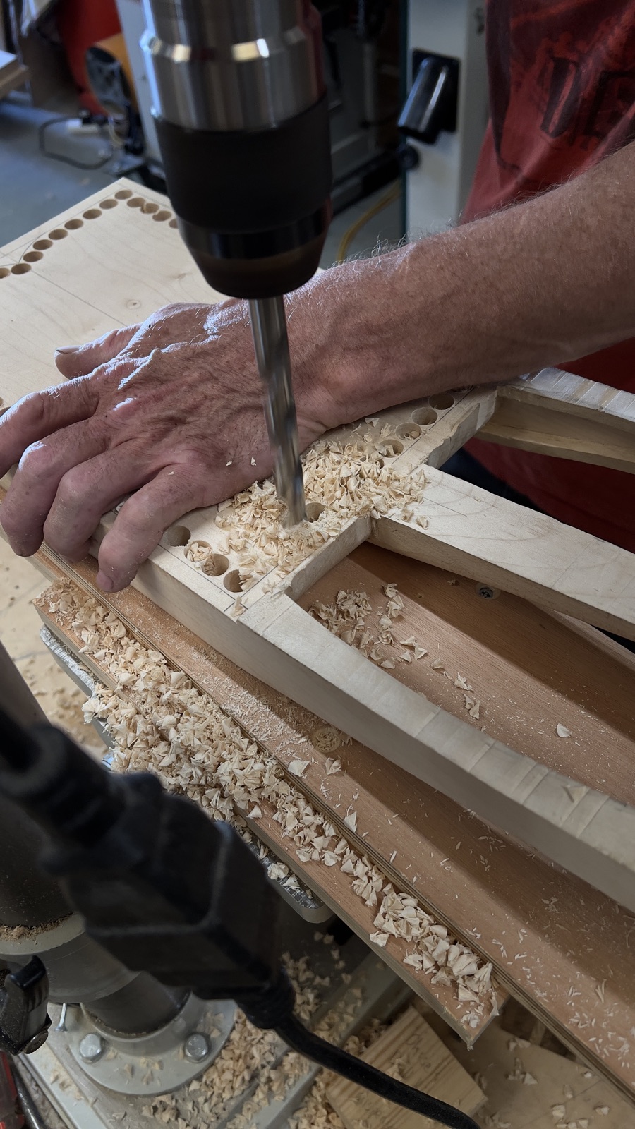 A crwth body being hollowed at the drill press, a grid of drilled holes and a scatter of pale shavings